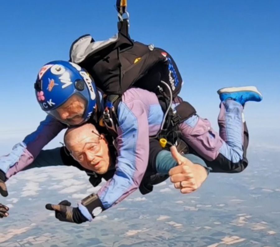 A picture of two men skydiving, one man is looking at the camera giving a thumbs up.